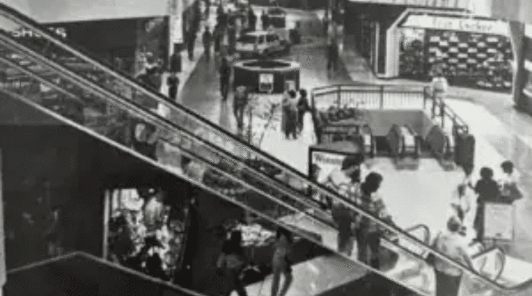 Historic Hawthorne shopping mall escalator scene, showing shoppers and storefronts in black and white.
