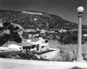 Iconic Hollywood Sign on the hillside with residential homes and a streetlamp in the foreground, representing Los Angeles' entertainment history.