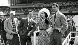 Vintage photo of stylishly dressed people at a racetrack event, showcasing mid-20th-century fashion and social gatherings.