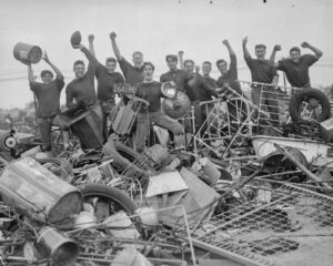 Vintage car and scrap metal pile with smiling young men celebrating.