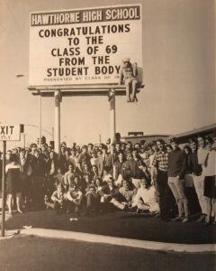 Group of students and a man sitting on a signboard at Hawthorne High School celebrating the Class of 1969.