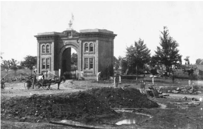 Historic Hawthorne building under construction, featuring early 20th-century architecture with a prominent archway and surrounding trees.