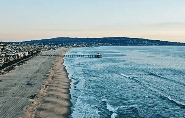 Aerial view of Hawthorne Beach with sandy shoreline, ocean waves, and a pier extending into the water, showcasing the scenic coastal landscape of Hawthorne.