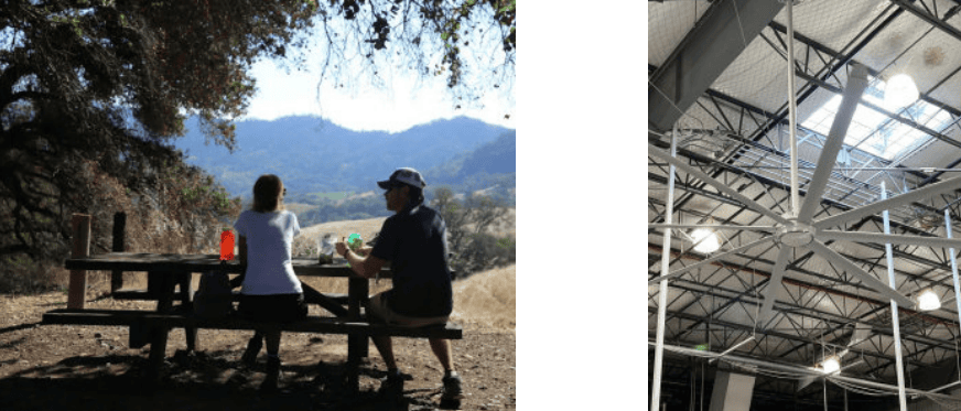 Two people sitting at a picnic table outdoors with mountains in the background, enjoying a sunny day.