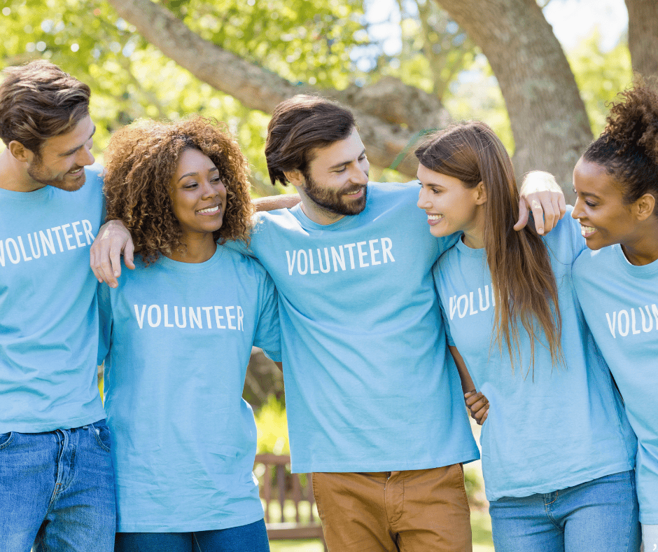 Group of diverse volunteers wearing Hawthorne Historical Society T-shirts, smiling and embracing outdoors, supporting community history initiatives.