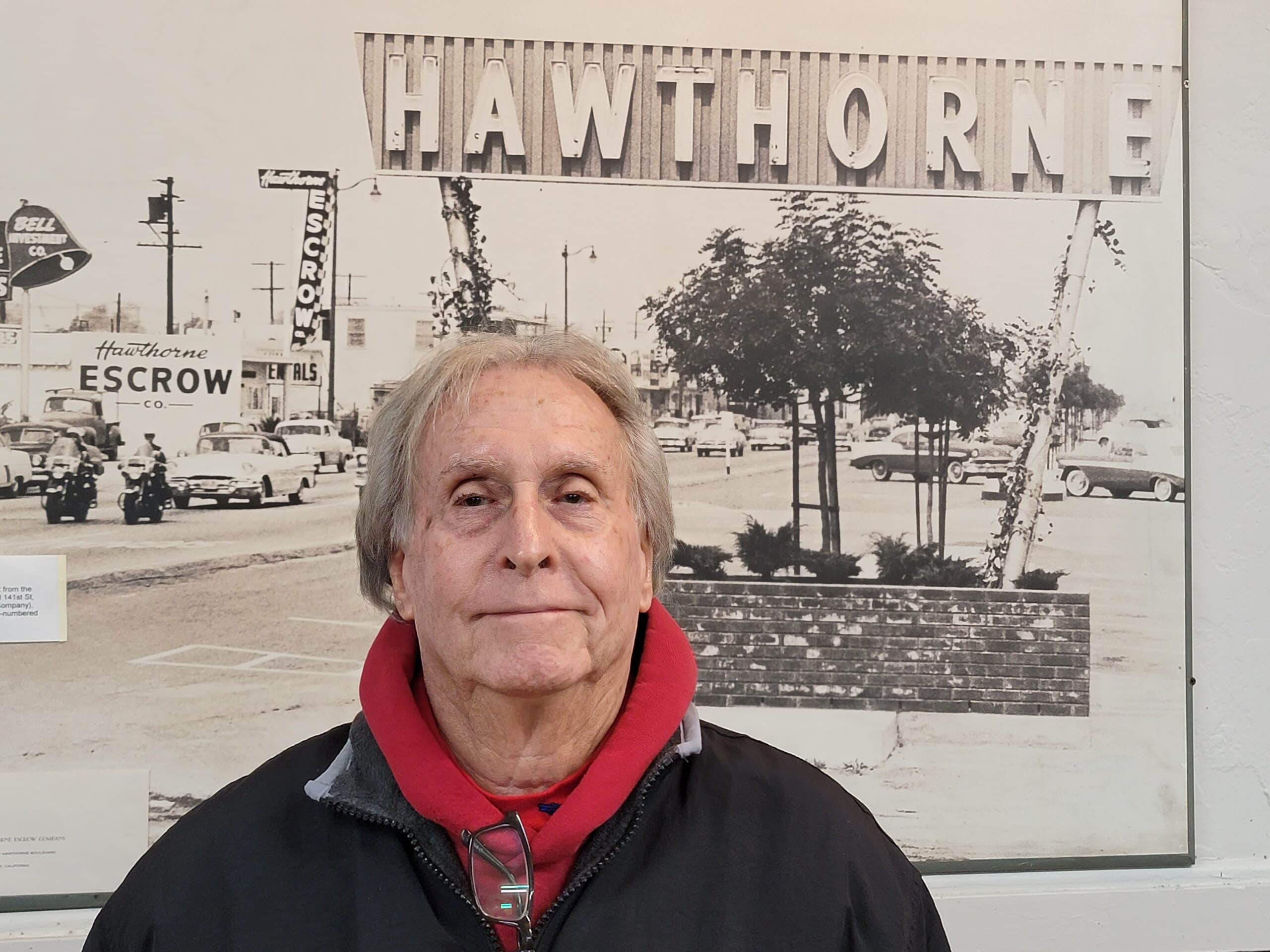 Portrait of an elderly man standing in front of the Hawthorne Historical Society sign, highlighting community history and local heritage.
