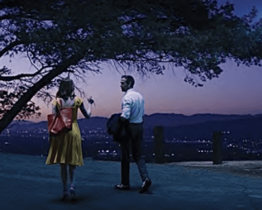Two people talking at dusk with a scenic city view in the background.