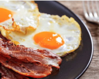 An image of a breakfast plate featuring sunny-side-up eggs and crispy bacon, highlighting local culinary traditions.
