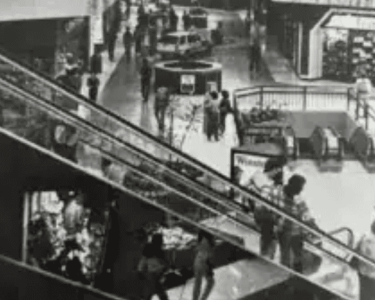 Historic Hawthorne shopping mall escalator scene, showing shoppers and storefronts in black and white.