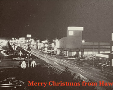 An image of a busy street scene at night with light trails from moving vehicles, illuminated buildings, and a festive message.