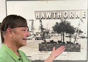 A man in a green shirt pointing to the Hawthorne Historical Society sign in an outdoor setting.