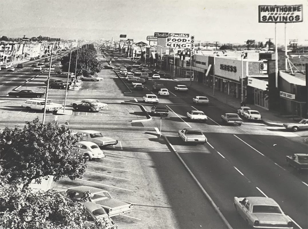 Historic black and white photo of Hawthorne shopping center parking lot with cars and stores, including Food King and Hawthorne Savings, showcasing mid-20th-century retail area.